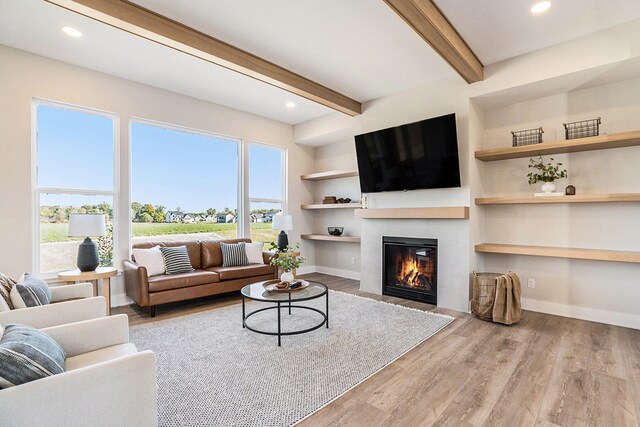 living room with built in shelves, light wood-type flooring, plenty of natural light, and beam ceiling