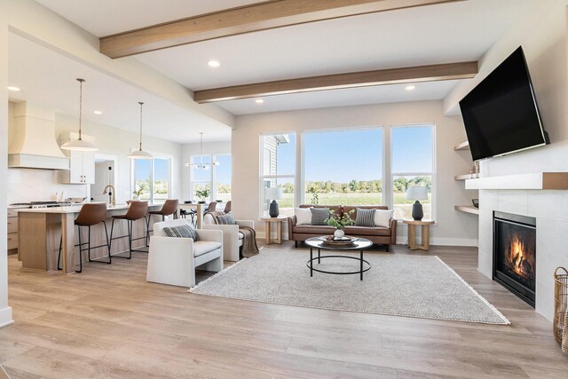 living room with light hardwood / wood-style floors, a tiled fireplace, sink, beam ceiling, and a notable chandelier