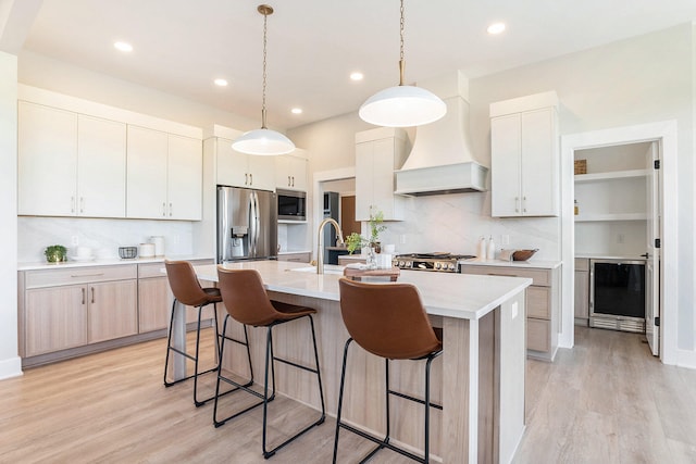 kitchen with a center island with sink, white cabinets, pendant lighting, appliances with stainless steel finishes, and premium range hood