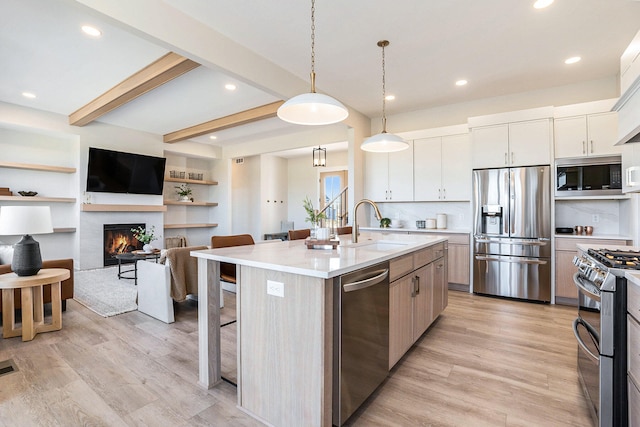 kitchen with white cabinets, stainless steel appliances, an island with sink, and light hardwood / wood-style flooring