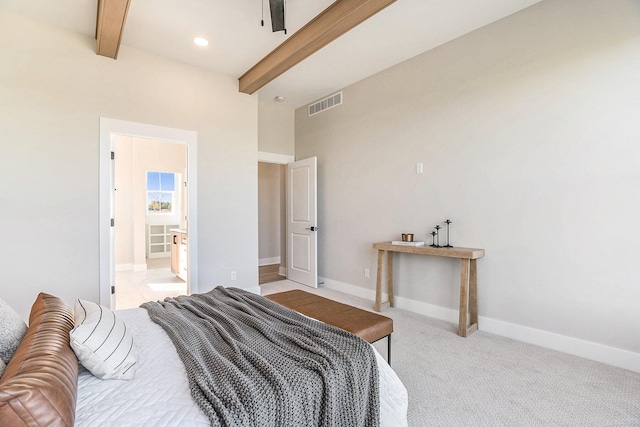 bedroom featuring ensuite bath, light colored carpet, and beam ceiling