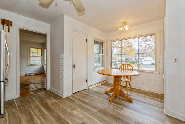 dining area featuring wood-type flooring, ceiling fan, and brick wall