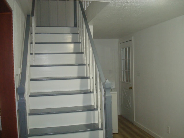 stairway with wood-type flooring and a textured ceiling