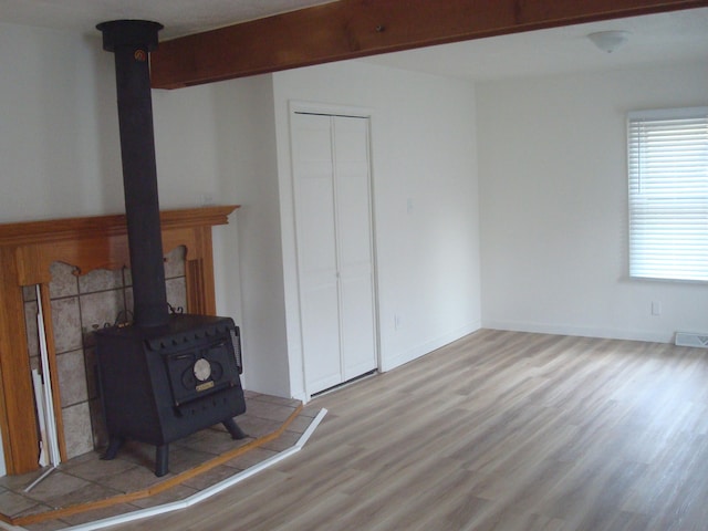 living room featuring beamed ceiling, light wood-type flooring, and a wood stove