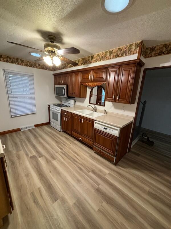 kitchen with sink, white range with gas stovetop, a textured ceiling, and light hardwood / wood-style flooring