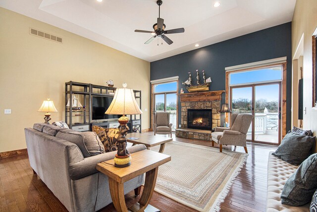 living room featuring hardwood / wood-style floors, ceiling fan, a fireplace, and a tray ceiling