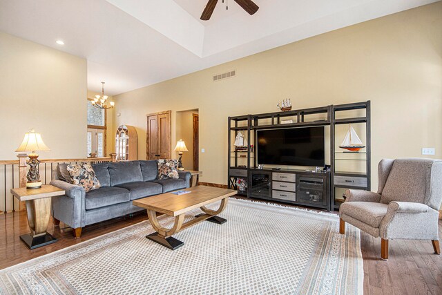 living room with ceiling fan with notable chandelier, wood-type flooring, and a high ceiling