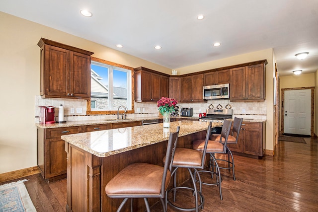 kitchen with light stone countertops, dark hardwood / wood-style flooring, stainless steel appliances, sink, and a center island