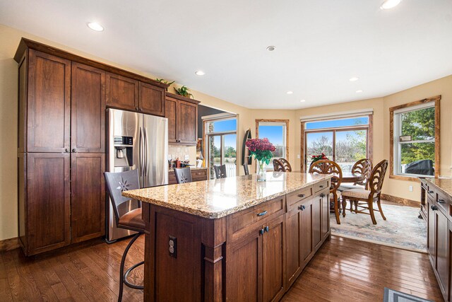 kitchen featuring stainless steel fridge, dark hardwood / wood-style floors, a center island, and light stone counters