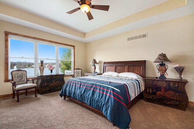 carpeted bedroom with a raised ceiling, ceiling fan, and a water view