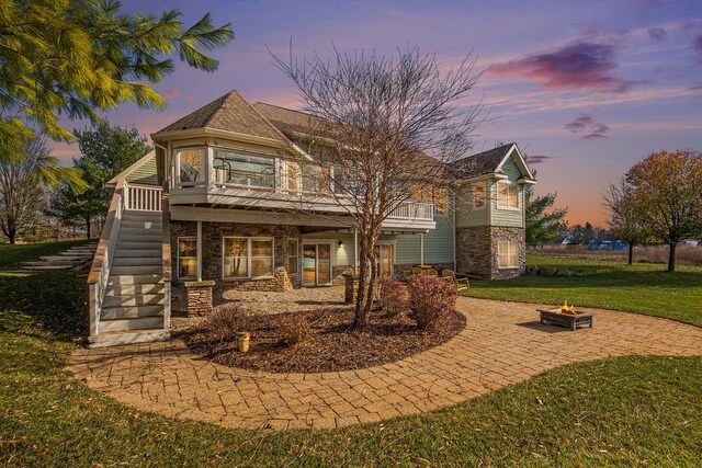 back house at dusk featuring an outdoor fire pit and a lawn