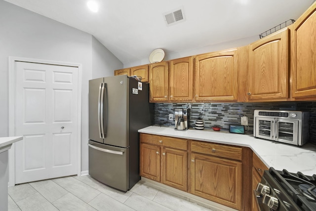 kitchen featuring light stone countertops, vaulted ceiling, decorative backsplash, light tile patterned floors, and appliances with stainless steel finishes