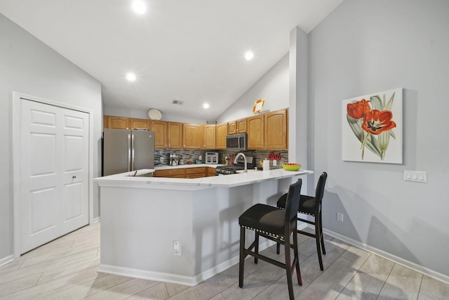 kitchen featuring kitchen peninsula, appliances with stainless steel finishes, backsplash, light wood-type flooring, and a breakfast bar area