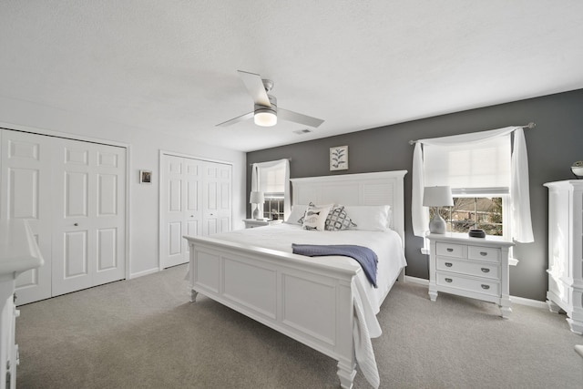 bedroom with light carpet, a textured ceiling, two closets, and ceiling fan