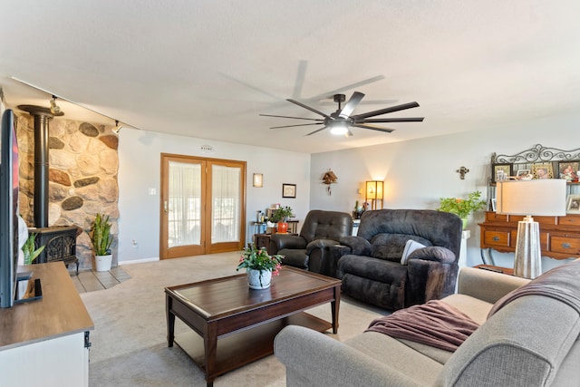 carpeted living room featuring ceiling fan, a wood stove, and french doors