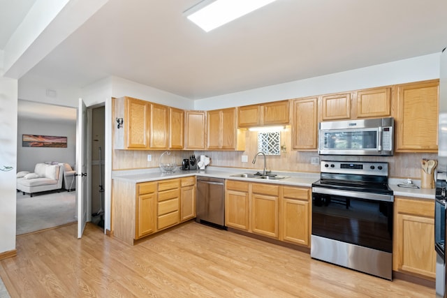 kitchen featuring appliances with stainless steel finishes, light wood-type flooring, tasteful backsplash, and sink