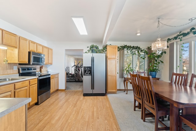 kitchen featuring beam ceiling, hanging light fixtures, light hardwood / wood-style floors, light brown cabinetry, and appliances with stainless steel finishes