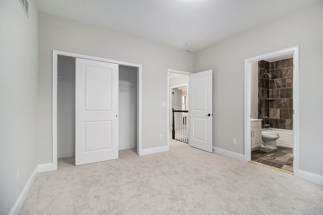 unfurnished bedroom featuring a closet, light colored carpet, and ensuite bath