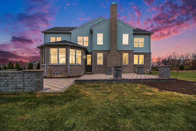 back house at dusk featuring a patio area and a lawn