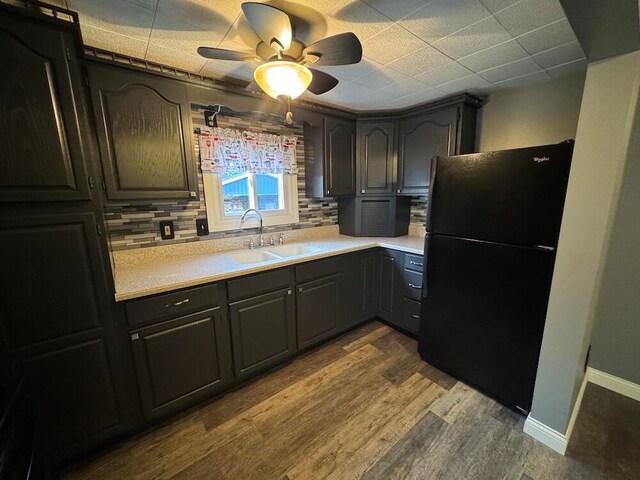 kitchen with wood-type flooring, black refrigerator, sink, ceiling fan, and backsplash