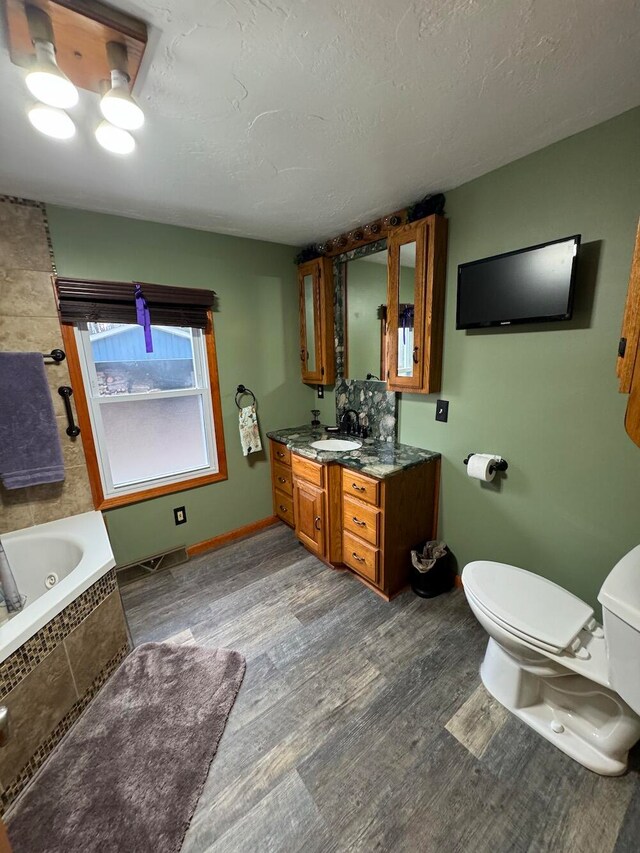 bathroom with a relaxing tiled tub, wood-type flooring, vanity, and toilet