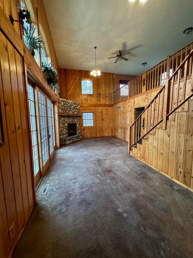 unfurnished living room featuring ceiling fan with notable chandelier, wooden walls, and dark carpet