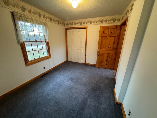 unfurnished bedroom featuring a textured ceiling, a closet, and dark colored carpet