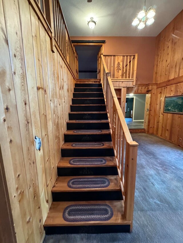 stairs with wood walls, carpet flooring, and a notable chandelier