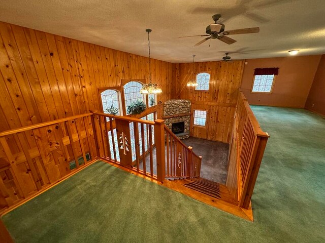 staircase featuring wood walls, carpet, a healthy amount of sunlight, and ceiling fan with notable chandelier