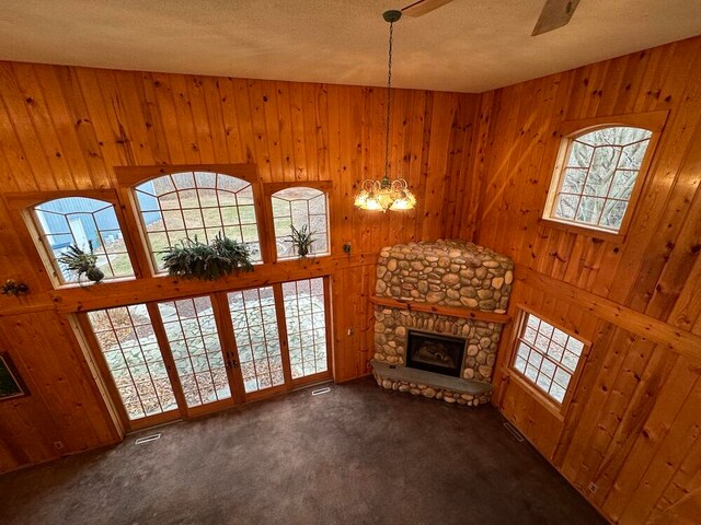 living room featuring an inviting chandelier, a fireplace, a towering ceiling, dark carpet, and wooden walls