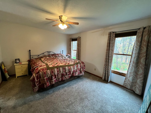 bedroom featuring a textured ceiling, dark carpet, multiple windows, and ceiling fan