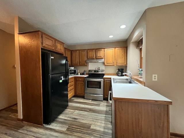 kitchen with kitchen peninsula, light wood-type flooring, a textured ceiling, stainless steel appliances, and sink