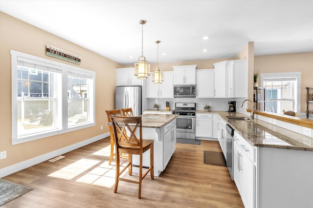 kitchen featuring stainless steel appliances, light hardwood / wood-style floors, hanging light fixtures, and white cabinets