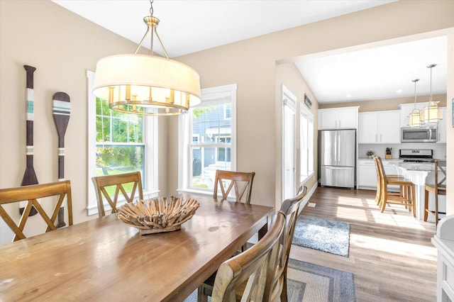 dining room featuring light wood-type flooring, vaulted ceiling, and an inviting chandelier