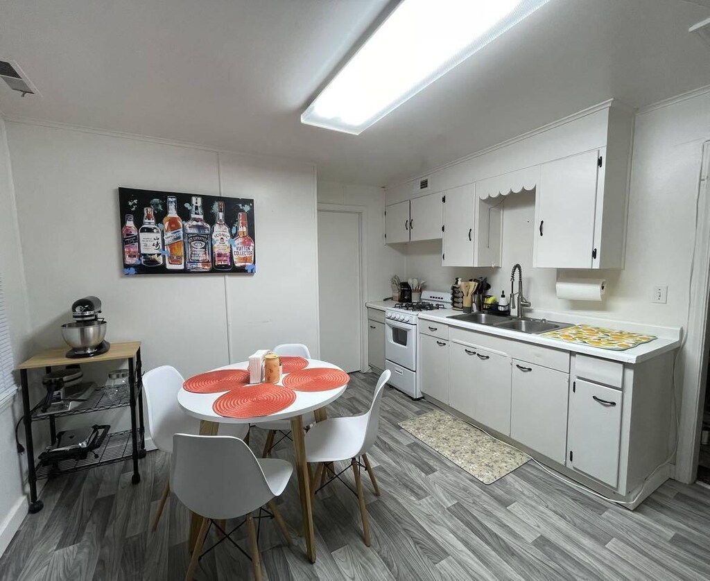 kitchen with white cabinets, white gas stove, light hardwood / wood-style floors, and sink