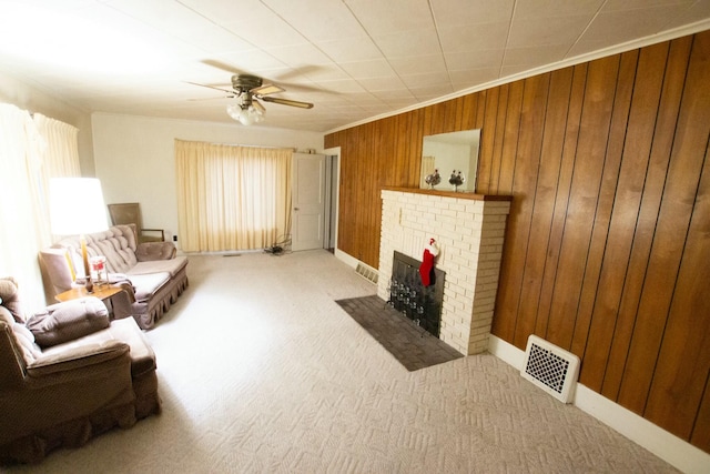 carpeted living room featuring wooden walls, ceiling fan, ornamental molding, and a brick fireplace