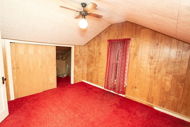 additional living space with dark colored carpet, vaulted ceiling, ceiling fan, and wooden walls