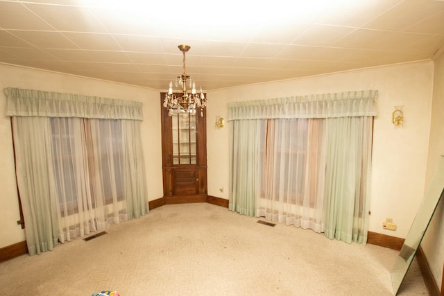 carpeted empty room featuring crown molding and a chandelier