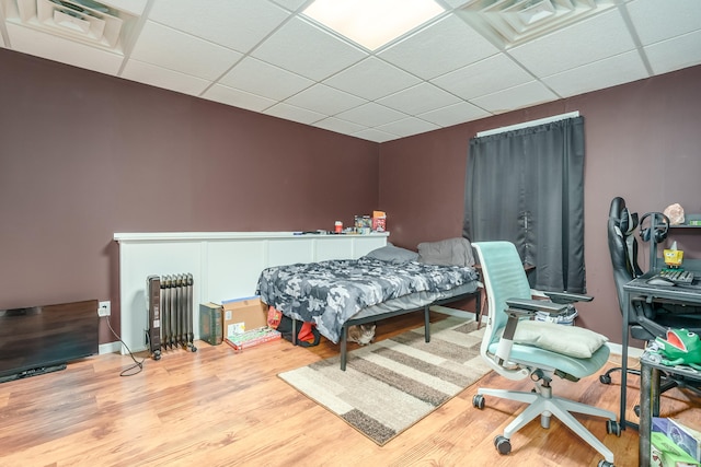 bedroom with hardwood / wood-style flooring, a drop ceiling, and radiator heating unit