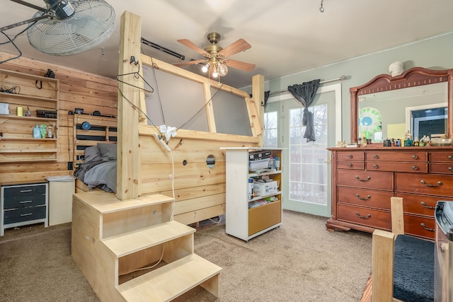 carpeted bedroom with ceiling fan and wood walls