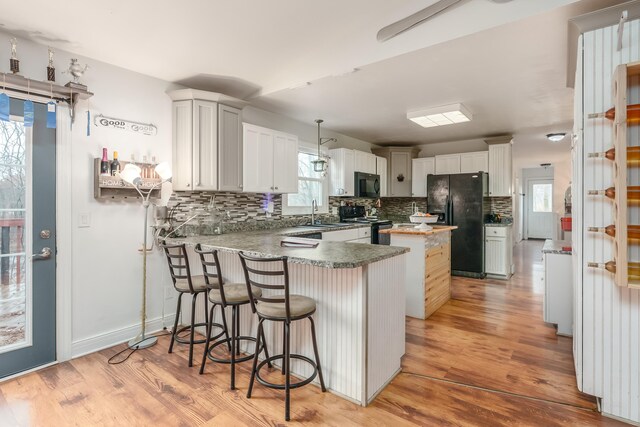 kitchen featuring light hardwood / wood-style flooring, backsplash, kitchen peninsula, white cabinets, and black appliances