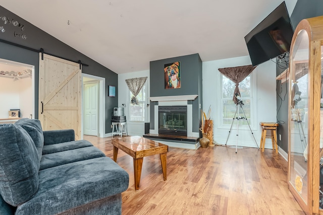 living room with a barn door, light hardwood / wood-style floors, and lofted ceiling