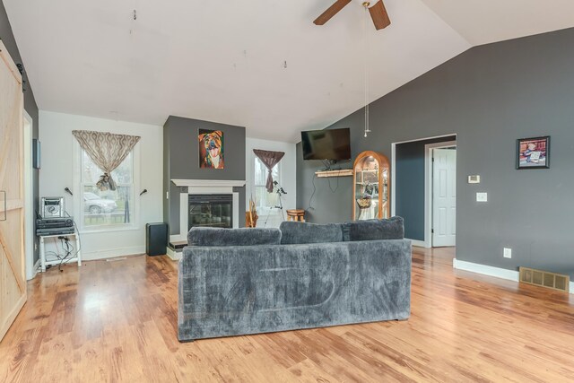 living room with a wealth of natural light, ceiling fan, light hardwood / wood-style floors, and vaulted ceiling