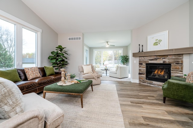 living room with light hardwood / wood-style floors, vaulted ceiling, ceiling fan, and a stone fireplace