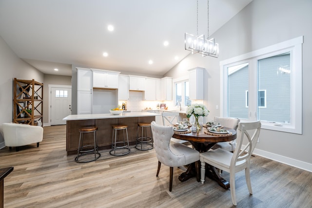 dining space with high vaulted ceiling, light hardwood / wood-style flooring, a notable chandelier, and sink