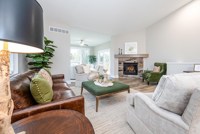 living room with light wood-type flooring, a stone fireplace, ceiling fan, and lofted ceiling