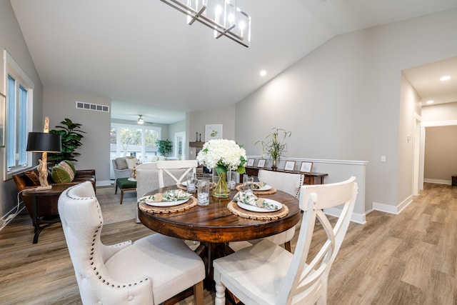 dining room featuring ceiling fan with notable chandelier, light hardwood / wood-style floors, and lofted ceiling