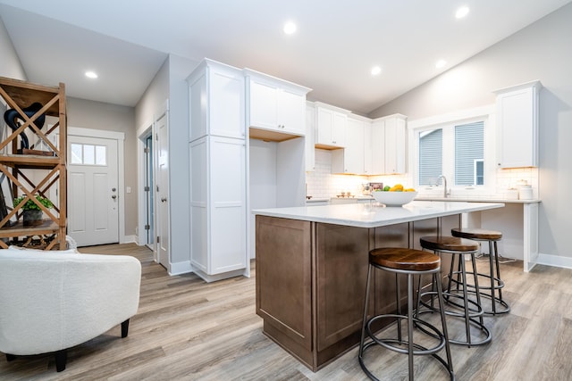 kitchen featuring white cabinets, a center island, light hardwood / wood-style floors, and lofted ceiling