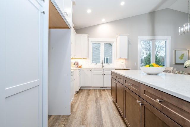 kitchen featuring white cabinets, light hardwood / wood-style flooring, hanging light fixtures, and lofted ceiling