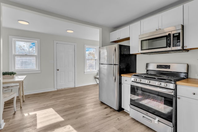 kitchen with wood counters, appliances with stainless steel finishes, white cabinetry, and a healthy amount of sunlight